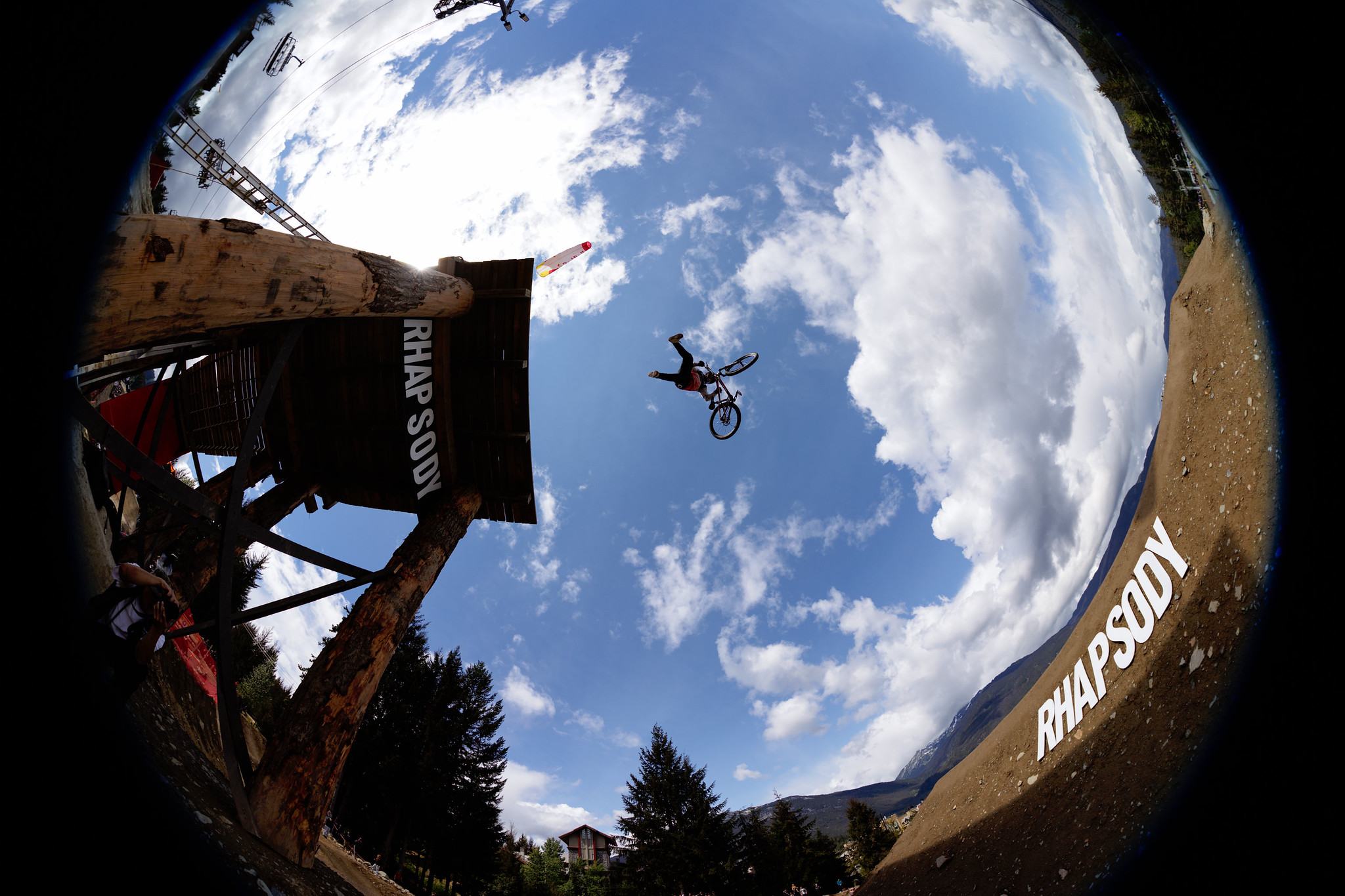 Fisheye view of a rider flipping off the Rhapsody start tower against a blue sky