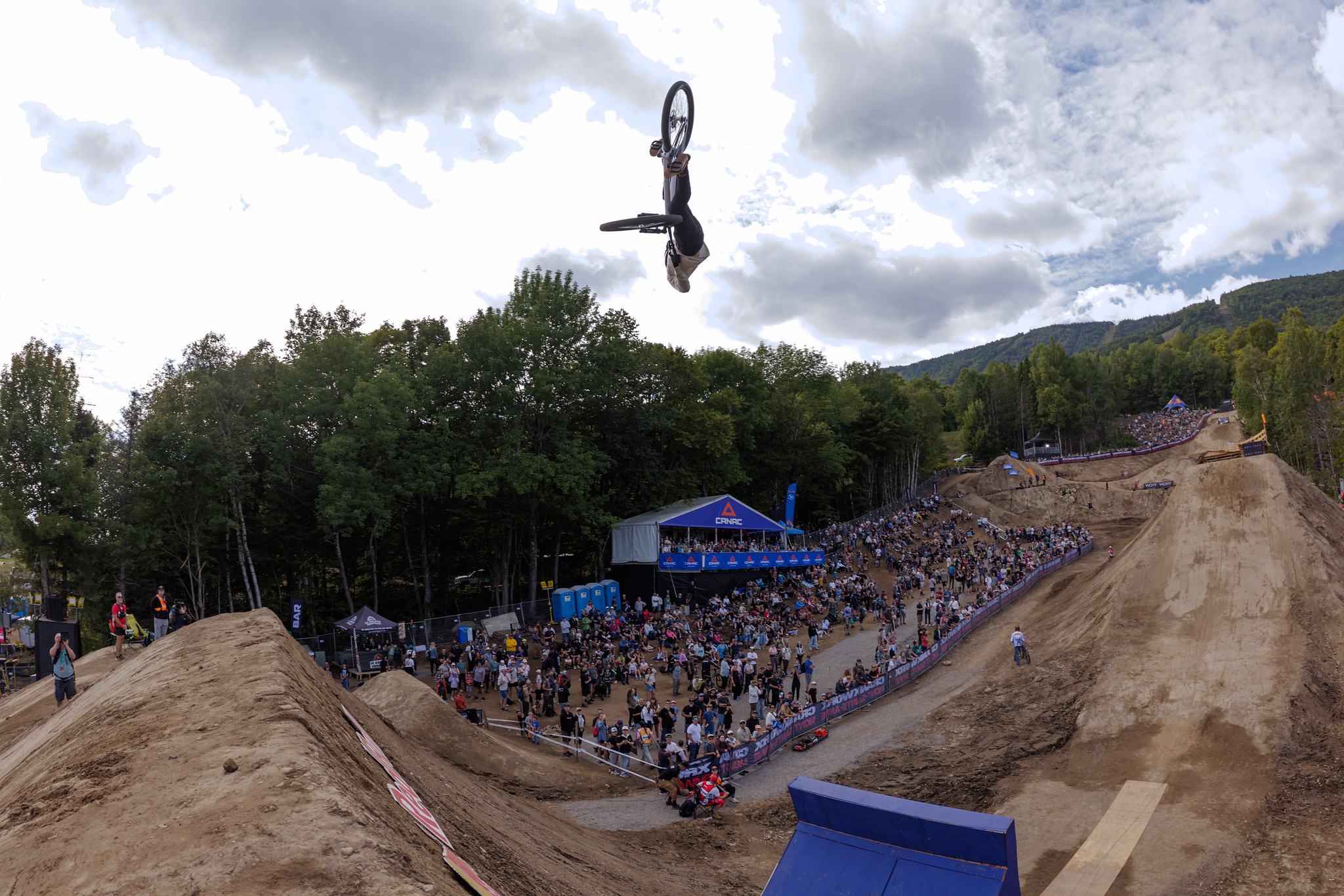 A rider backflips high above a packed slopestyle crowd at Crankworx Mont-Sainte-Anne